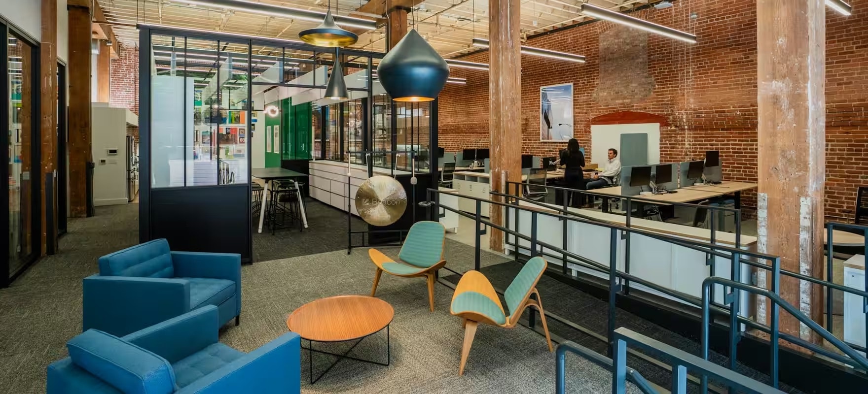 The Beacon office: a brick-and-steel floor of desks, with seating in the foreground.